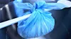 A blue cheesecloth bag filled with curds is suspended over a metal bowl, with a white utensil holding it in place. Produktbild-Vorschau