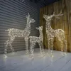 Three illuminated reindeer figures of varying sizes are displayed on a wooden floor against a grey slatted wall and a wooden plank wall. Produktbild-Vorschau