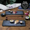 A sushi set laid out on a wooden table with various sushi pieces, chopsticks, and dipping sauce. Produktbild-Vorschau