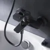 A black bathtub faucet mounted on a gray tiled wall above a white bathtub. Produktbild-Vorschau