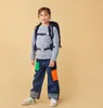 A young girl wearing a backpack and jeans stands against a plain background. Anteprima dell’immagine prodotto