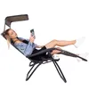 A woman is relaxing in a black reclining chair with a canopy, holding a smartphone and wearing headphones. Produktbild-Vorschau