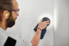 A man is sanding a wall with a power tool. Voir les images du produit