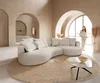 A woman stands in a modern living room with a curved sofa and a round rug.