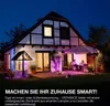 A house at night with smart lighting illuminating the exterior and interior, with people sitting under an umbrella on the patio. Produktbild-Vorschau