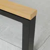 A close-up view of the corner of a piece of outdoor furniture, showing the junction of a wooden top and a black metal frame. Produktbild-Vorschau