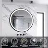 A round LED bathroom mirror with a black frame is mounted on a marble-tiled wall. Below the mirror are icons and text describing its features. Produktbild-Vorschau