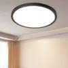 A modern, round LED ceiling light fixture with a black frame is mounted on a white ceiling in a room with beige walls and sheer curtains. Voir les images du produit