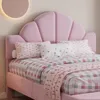 A close-up view of a pink upholstered bed with a shell-shaped headboard and patterned bedding. Produktbild-Vorschau