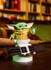 A Grogu figurine holding a remote control stand on a wooden table, with bookshelves in the background. Anteprima dell’immagine prodotto