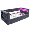 A gray upholstered bed frame with built-in shelves and drawers, illuminated by pink LED lights. Náhled obrázku produktu