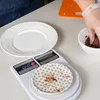 A person's hands are seen weighing chocolate sprinkles on a digital scale, with two plates and an orange cutting board in the background. Voir les images du produit