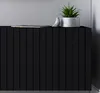 A close-up view of a black TV cabinet with decorative vertical slats, featuring a small potted plant and a decorative bird on top. Produktbild-Vorschau