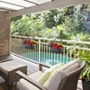 A balcony with outdoor furniture and hanging planters overlooking a lush garden and pool. Produktbild-Vorschau