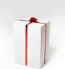 A tall, white gift box with a red ribbon and bow is centered against a plain white background. Podgląd zdjęcia produktu