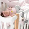A baby sleeping in a crib with a toy hanging from the side. Produktbild-Vorschau