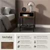 A bedside table next to a bed, with a lamp and clock on top. Náhled obrázku produktu
