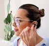 A woman wearing glasses and earbuds, with a plant in the background. Produktbild-Vorschau