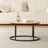 A round coffee table with a wood top and black metal frame is placed on a rug in front of a sofa. Produktbild-Vorschau