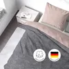 A close-up view of a bed with bedding, a bedside table, and a window in the background. Produktbild-Vorschau