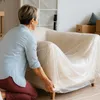 A woman is covering a chair with plastic sheeting. Produktbild-Vorschau