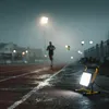 A person running on a track at night, illuminated by a portable work light. Anteprima dell’immagine prodotto