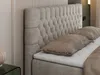 A close-up view of a beige upholstered boxspring bed with a tufted headboard and pillows. Produktbild-Vorschau