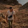 A man hiking on a dry, rocky hillside with the ocean in the background. Produktbild-Vorschau