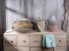 A stack of plates and mugs on a wooden dresser. Produktbild-Vorschau