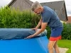 A man is putting a cover on an oval pool. Produktbild-Vorschau