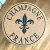 A round cork stool with a fleur-de-lis symbol and text reading "CHAMPAGNE FRANCE" printed on it, placed on a wooden floor. Produktbild-Vorschau
