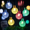 Solar-powered string lights with colorful bulbs are displayed on grass at night, with a solar panel visible. Produktbild-Vorschau