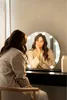 A woman is looking at herself in a lighted vanity mirror. Produktbild-Vorschau
