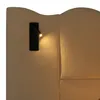 A close-up view of a beige upholstered headboard with a black reading lamp attached. Produktbild-Vorschau