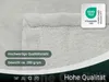 A close-up of a light gray, soft blanket with a stitched edge and a certification label. Produktbild-Vorschau