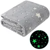 A folded grey blanket with white stars is shown against a white background. A circular inset shows a close-up of the blanket's pattern glowing green in the dark. Anteprima dell’immagine prodotto