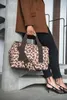 A person holding a leopard-print duffel bag while sitting on stairs. Náhled obrázku produktu