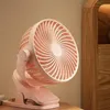 A close-up shot of a pink clip-on fan sitting on a wooden surface, next to a wooden cabinet. Produktbild-Vorschau