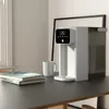 A white instant hot water dispenser sits on a black desk next to a stack of books and a white mug. Produktbild-Vorschau