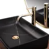 A close-up shot of a black marble-effect rectangular basin with a gold faucet and drain. Produktbild-Vorschau