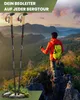 A person stands on a rocky mountain peak, looking out at a scenic landscape, with hiking poles in the foreground. Produktbild-Vorschau