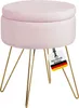 A pink velvet ottoman with gold hairpin legs, featuring a tag with German flag colors and text.