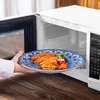 A hand is placing a plate of spaghetti and vegetables into a microwave. Produktbild-Vorschau