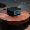 A black projector is placed on a round wooden coffee table, with a beam of light projecting from it. Anteprima dell’immagine prodotto