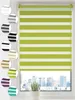 A close-up view of a green and white striped roller blind hanging in a window, with a cityscape visible through the window. Produktbild-Vorschau
