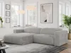 A modern living room with a light gray cord sofa, large windows, and artwork on the wall.