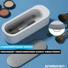 A white makeup brush cleaner sits on a light blue surface, surrounded by makeup products and brushes. Text overlays highlight product features. Produktbild-Vorschau
