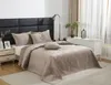 A neatly made bed with a beige quilted bedspread and pillows, set in a bedroom with a nightstand and a floor lamp. Podgląd zdjęcia produktu