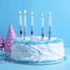 A birthday cake with lit candles and party hats in the background. Anteprima dell’immagine prodotto