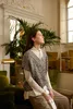 A woman sits in a well-lit room with plants and furniture, holding a magazine. Produktbild-Vorschau